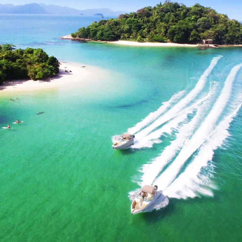 Duas lanchas em paralelo, em velocidade, navegando pelas águas verde-esmeralda próximo das Ilhas de Cataguás.